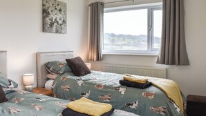 A bedroom with two beds, a window with curtains, a radiator, and a painting on the wall. - 4 bedroom accommodation in Corwen (Corwen)