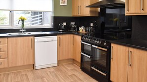 A modern kitchen with wooden cabinets, a black stove, and a dishwasher. - 4 bedroom accommodation in Corwen (Corwen)