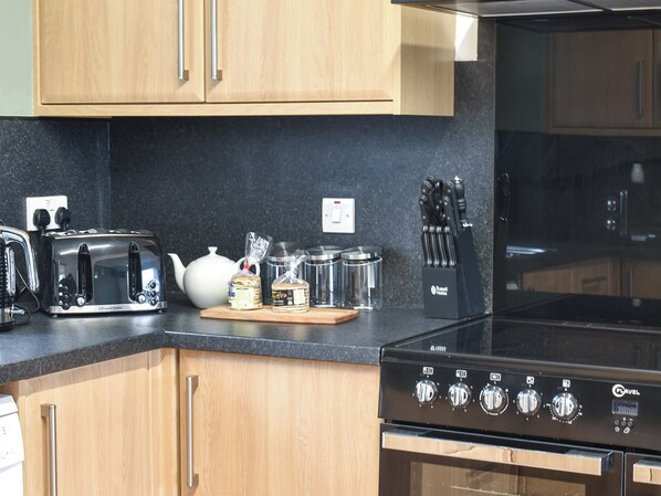 A modern kitchen with wooden cabinets, a black countertop, a toaster, a kettle, a knife block, and a stove.