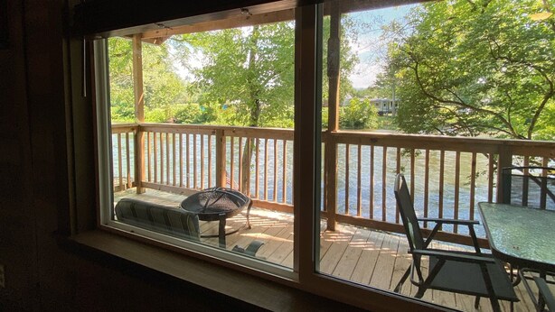 Quarto com uma grande janela com vista para um deck de madeira com mobiliário de exterior.