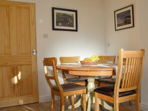 Un comedor con una mesa de madera, cuatro sillas y una cesta de fruta.