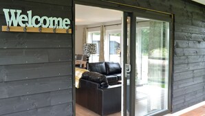 Ein moderner Gebäudeeingang mit einem "Welcome"-Schild, eine Schiebetür zu einem Wohnbereich mit einer Couch und einem Tisch.