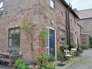 A brick building with a blue door, outdoor seating, and potted plants.