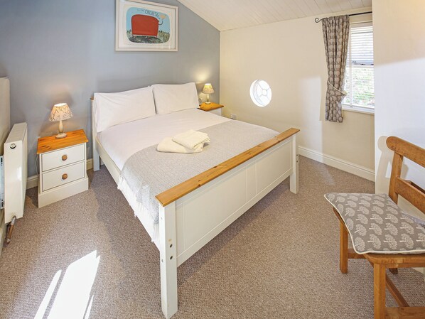A bedroom with a bed, bedside tables, a chair, a window with curtains, a radiator, and a wall-mounted picture.