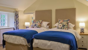 A bedroom with two beds, each with a blue bedspread, a floral pillow, and a bedside table with a lamp. - Two bedroom cottage packed with character with stone floors and wood burner. (Hawnby, near Helmsley)
