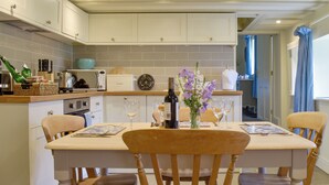 A kitchen with white cabinets, a wooden table, and chairs. There are wine glasses, a bottle, and a vase with flowers on the table. - Two bedroom cottage packed with character with stone floors and wood burner. (Hawnby, near Helmsley)
