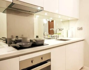 A modern kitchen with white cabinets, a stainless steel range hood, a double sink, and a microwave.