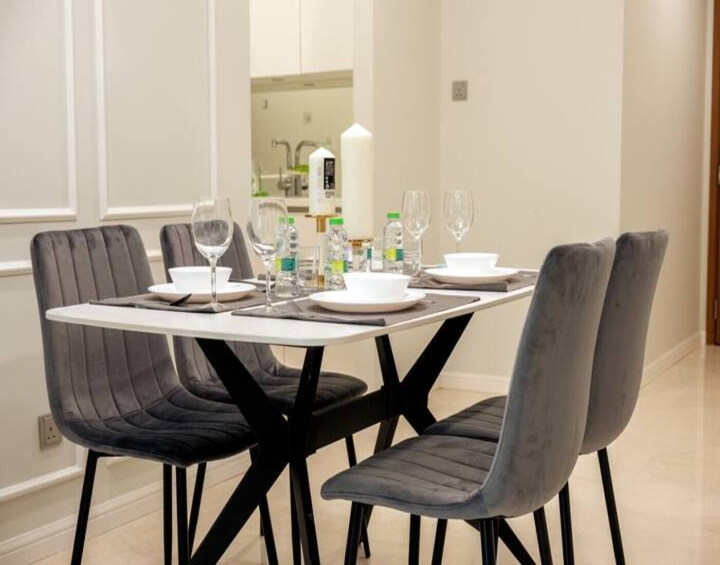 Une table à manger dressée avec des assiettes, des verres et des couverts, entourée de chaises rembourrées.