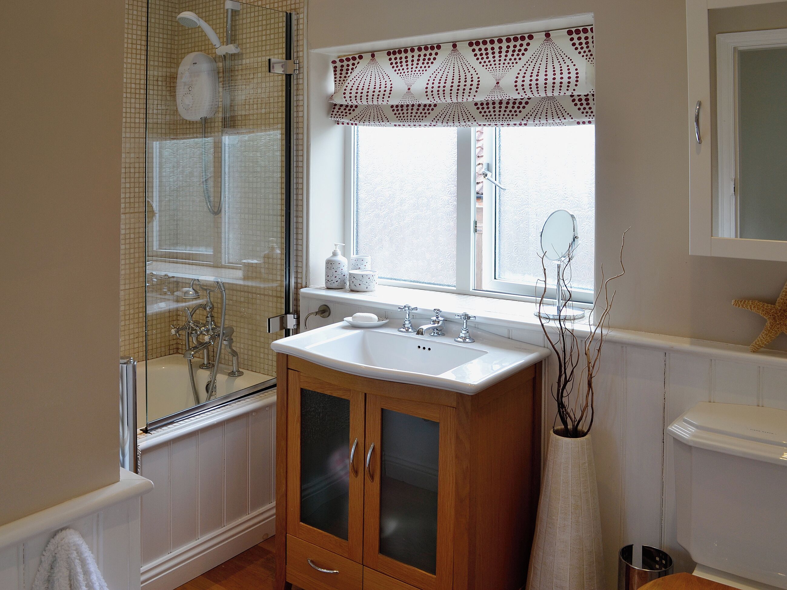 A bathroom with a bathtub, a sink, and a toilet. There is a window with a lace curtain and a starfish decoration.