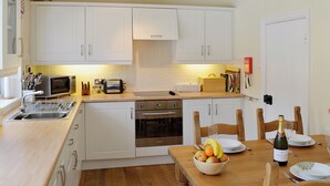 Una cocina con armarios blancos, microondas, tostadora y una mesa de comedor de madera con sillas.