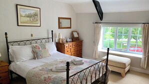 Un dormitorio con una cama, un aparador de madera, un ventanal con cortinas y un cuadro en la pared.