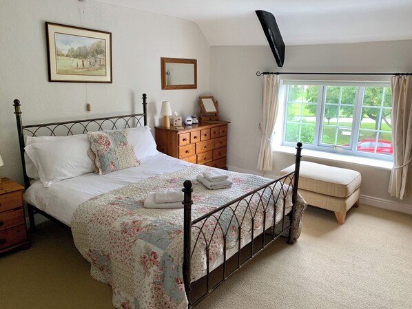 Une chambre à coucher avec un lit, une commode en bois, une fenêtre avec des rideaux et un tableau accroché au mur.