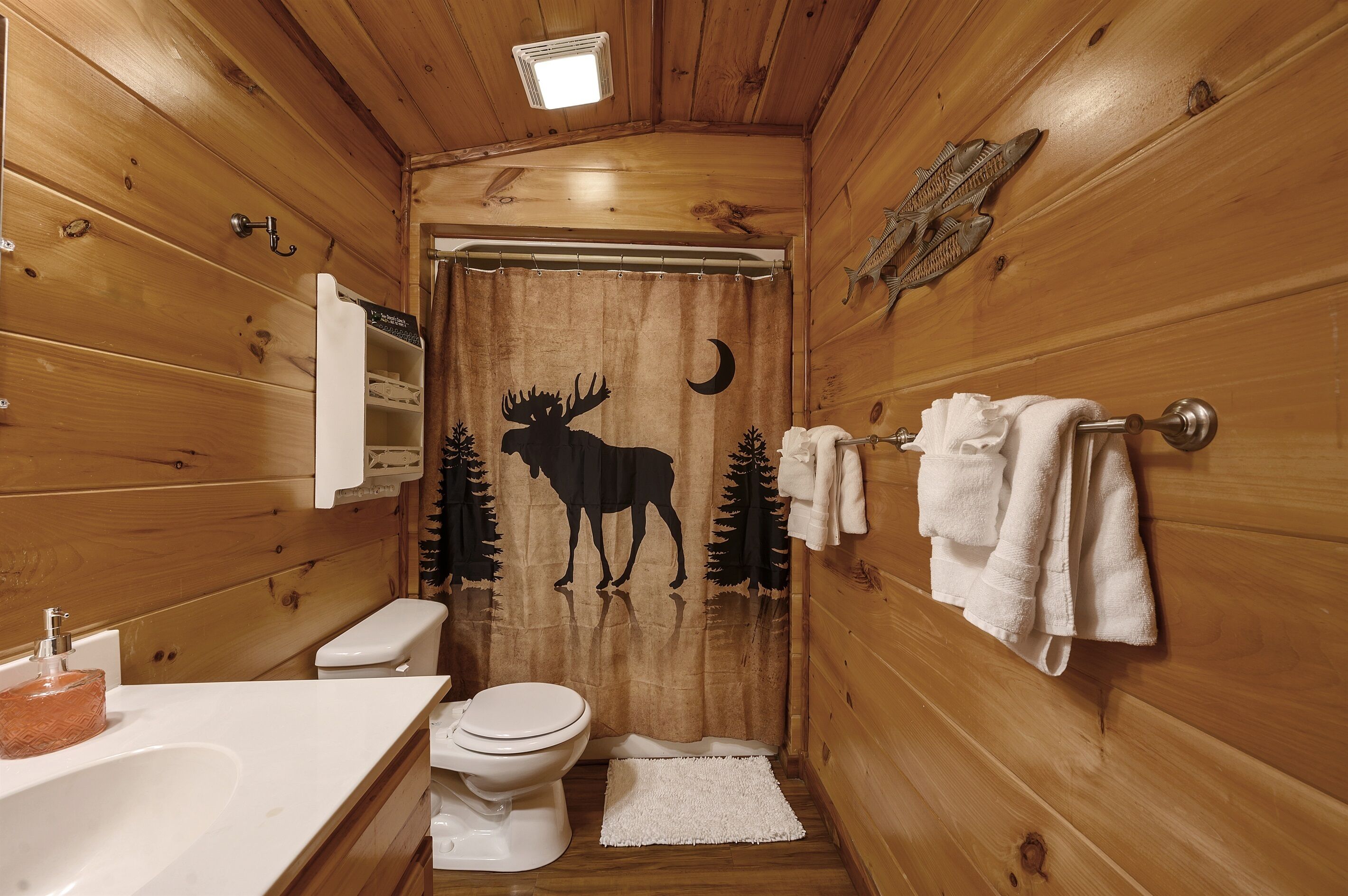 Bagno di una cabina di legno con toilette, lavabo e tenda da doccia con decoro a tema alce.