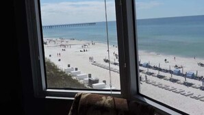Blick auf einen Strand aus einem Fenster, mit Meerblick und einem Pier in der Ferne.