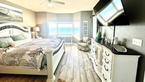 Ein Schlafzimmer mit Bett, Schreibtisch, Sessel, Fernseher und Meerblick.