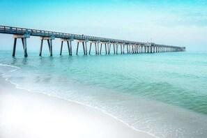 A pier extending into calm waters with a beach on one side.