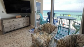 Ein Balkon mit Meerblick, ein Fernseher an der Wand und eine Sitzecke mit Stühlen.