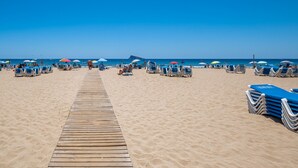 A beach with a wooden walkway leading to the water, rows of blue lounge chairs, and umbrellas. - Copacabana Deluxe 1-A  Levante Beach (Benidorm)