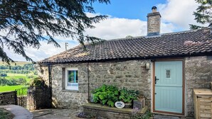 A stone cottage with a tiled roof, a small window, and a light blue door. - The best things certainly come in small parcels and Bloomer’s Bothy has it all. (Woodhall, near Askrigg)