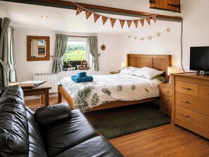 Een slaapkamer met een bed, een houten hoofdeinde, een televisie, een dressoir, een raam met gordijnen en een spiegel.