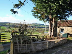A stone building with a tiled roof, surrounded by a stone wall and a metal gate.