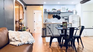 A cozy living room with a brown leather couch, a wooden door, and a dining area with a table and chairs. - Lakewoods Cottage (Howard)