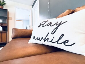 Un coussin blanc avec du texte noir, posé sur un canapé en cuir marron.