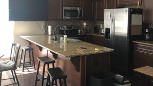 Une cuisine moderne avec des meubles en bois foncé, des appareils électroménagers en acier inoxydable et un îlot central en granit.