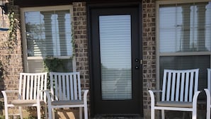 Une maison en briques avec une porte d’entrée sombre, deux bancs blancs et un paillasson.