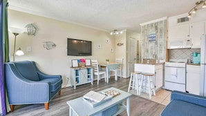 A compact living space with a sofa, dining table, kitchen area, and a flat-screen TV.