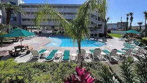 A pool area with lounge chairs and umbrellas, surrounded by a building with multiple floors and balconies.