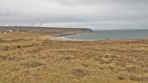A coastal landscape with a beach, grassy terrain, and a few houses in the distance.