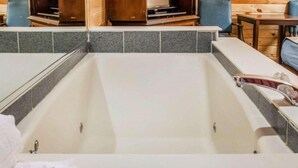 A modern bathroom with a large bathtub, a wooden vanity, and a blue chair. - Mackinac Lodge (Mackinaw City)