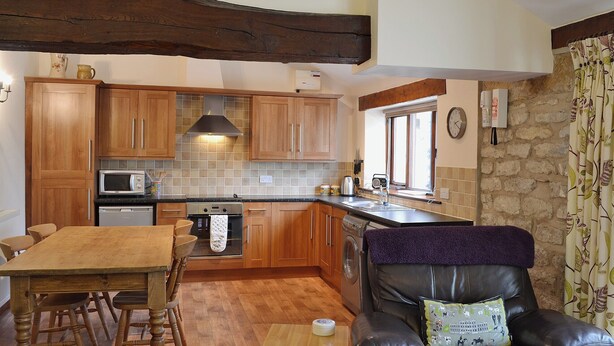 A cozy kitchen with wooden cabinets, a dining table, and a leather chair with a cushion.