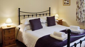 A neatly made bed with white linens and purple pillows, two bedside tables with lamps, and a floral curtain.
