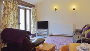 A living room with a leather sofa, a wooden coffee table, a television, and a radiator.