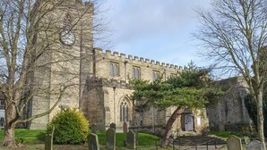 A historic stone building with a tall tower, a cemetery with headstones, and a well-maintained lawn.