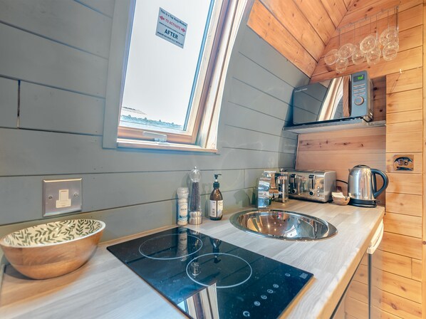 Una cocina moderna con interior de madera, un ventanal grande, un microondas empotrado, un hervidor y un bol en la encimera.