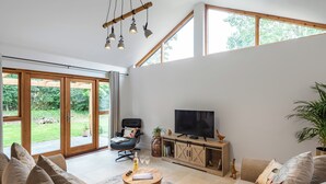 Un salon spacieux doté d’un grand téléviseur, de sièges confortables et d’une porte-fenêtre coulissante donnant sur un jardin.