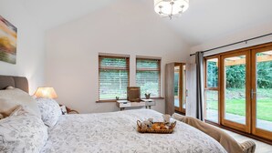 Une chambre avec un grand lit, une table de chevet, une lampe, une fenêtre avec des stores et une vue sur l’extérieur.