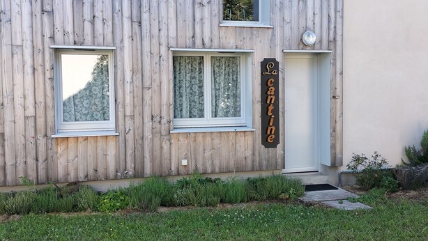 A modern building with a wooden facade, a small entrance, and a sign that reads "La cantine". - Appartement au Calme Proche des Commerces au Bord de la Loire (Decize)