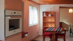 A kitchen with a built-in oven, a dining table with chairs, a bookshelf, and a window with curtains. - Appartement au Calme Proche des Commerces au Bord de la Loire (Decize)