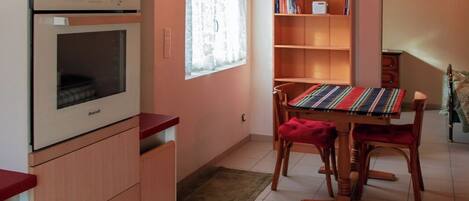 Een keuken met een ingebouwde oven, een eettafel met stoelen, een boekenkast en een raam met gordijnen.