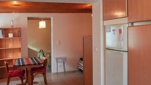 A compact kitchen with a refrigerator, wooden cabinets, a dining table with chairs, and a bookshelf. - Appartement au Calme Proche des Commerces au Bord de la Loire (Decize)