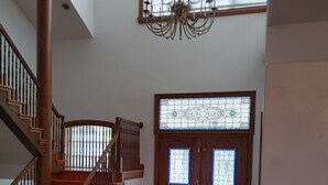 A spacious interior with a wooden staircase, a chandelier, and a large stained glass door.