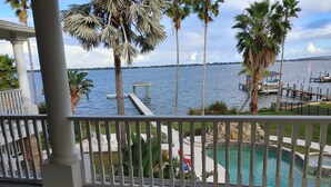 A wooden deck with a pool, palm trees, and a view of the water.