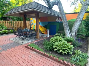 Relax in a serene outdoor seating area surrounded by lush greenery and a vibrant mural.