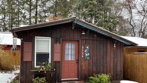 A wooden cabin with a red door, a small porch, and a mailbox.
