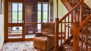A spacious room with a large window, a wooden staircase, and a plush armchair.
