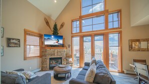 A spacious living room with a stone fireplace, large windows, and a cozy seating area. - Antlers Gulch 104 (Keystone)